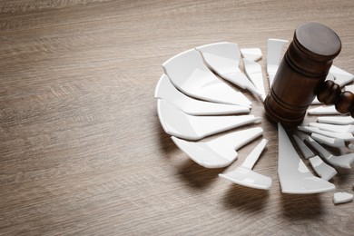 Divorce concept. Broken plate and gavel on wooden table, closeup with space for text