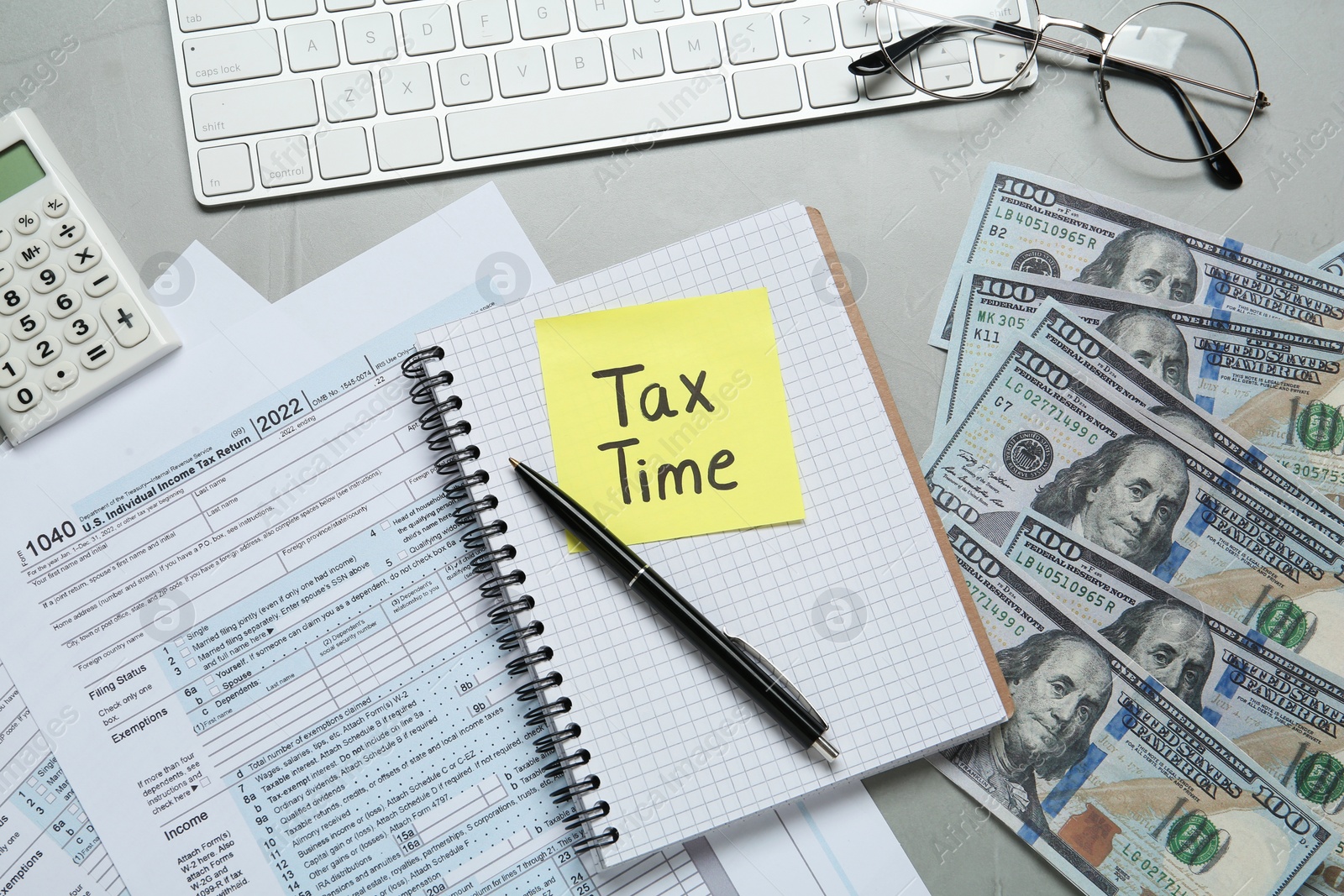 Photo of Reminder note with words Tax Time, documents, money and computer keyboard on grey table, flat lay