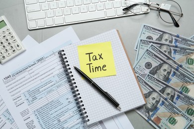 Reminder note with words Tax Time, documents, money and computer keyboard on grey table, flat lay