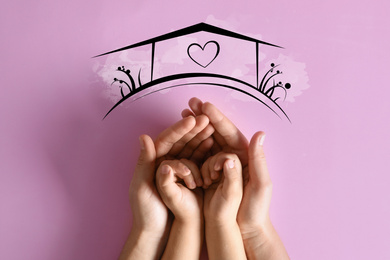 Mother holding hands with child and illustration of house on pink background, top view. Adoption concept