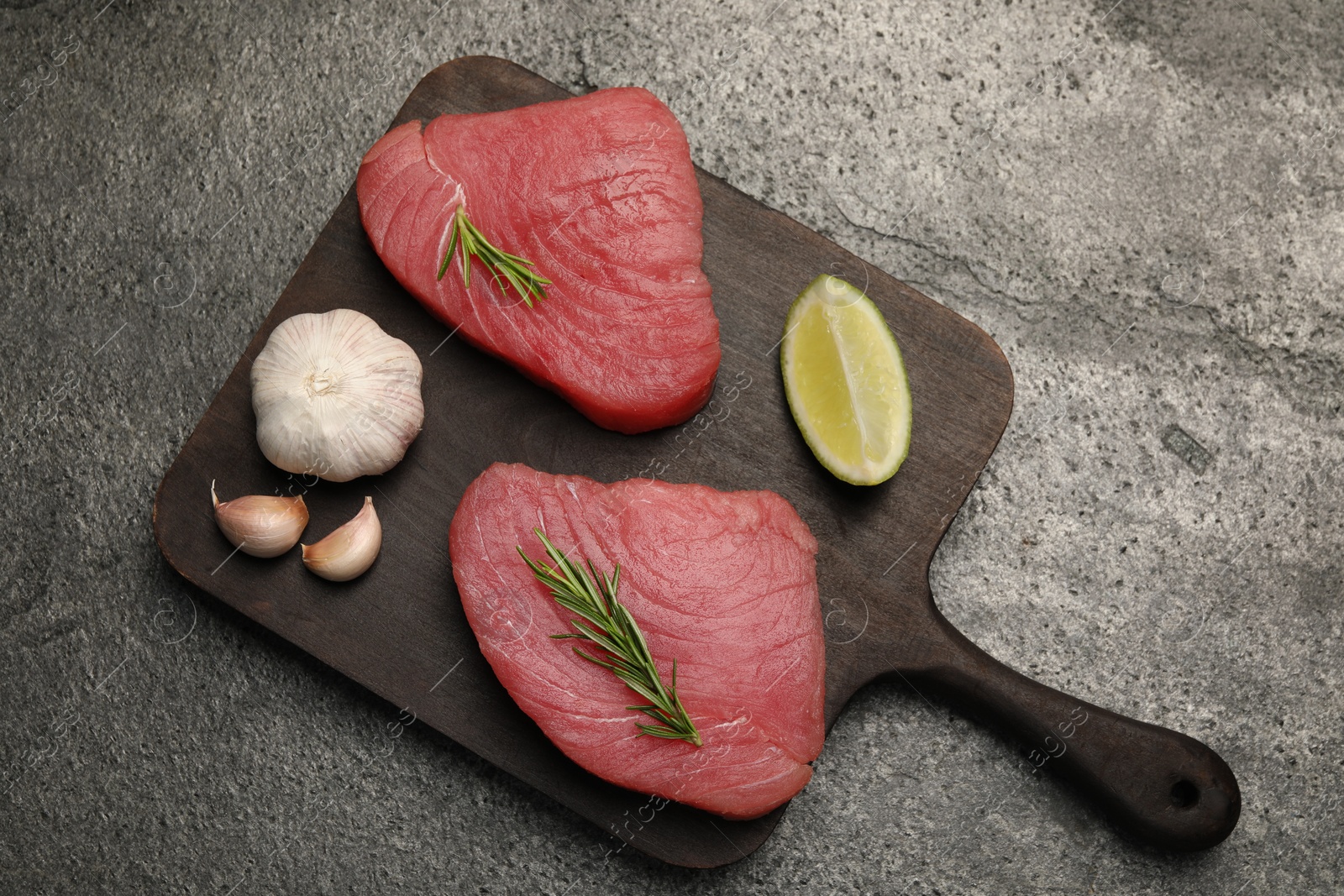 Photo of Raw tuna fillets with rosemary, lime and garlic on gray table, top view
