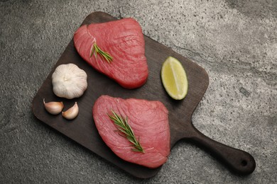 Raw tuna fillets with rosemary, lime and garlic on gray table, top view