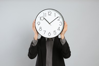 Businesswoman holding clock on light grey background. Time management