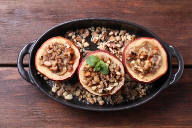 Photo of Tasty baked apples with nuts, honey and mint in baking dish on wooden table, top view