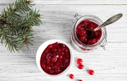 Bowl and jar with tasty cranberry sauce on white wooden background, flat lay