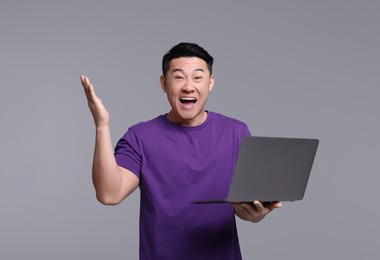 Emotional man with laptop on grey background