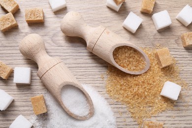 Photo of Scoops with different types of sugar on wooden table, flat lay