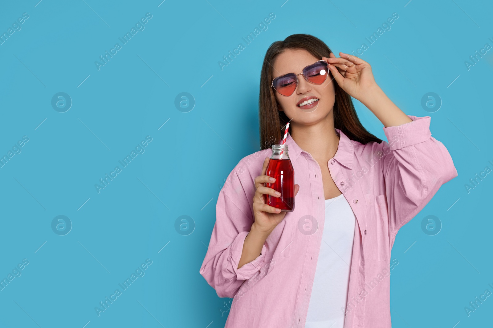 Photo of Beautiful young woman with glass bottle of juice on light blue background. Space for text