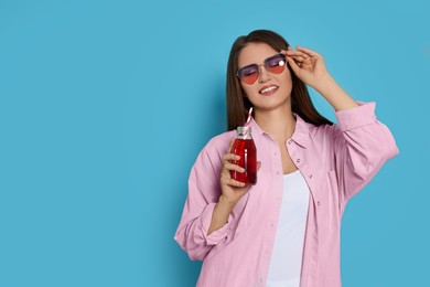 Beautiful young woman with glass bottle of juice on light blue background. Space for text