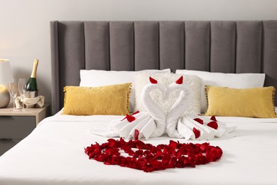 Honeymoon. Swans made with towels and heart of beautiful rose petals on bed in room