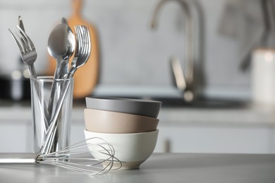 Photo of Set of eating utensils, balloon whisk and bowls on grey table in kitchen. Space for text