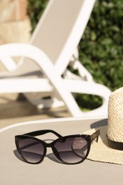 Photo of Stylish hat and sunglasses on grey sunbed outdoors