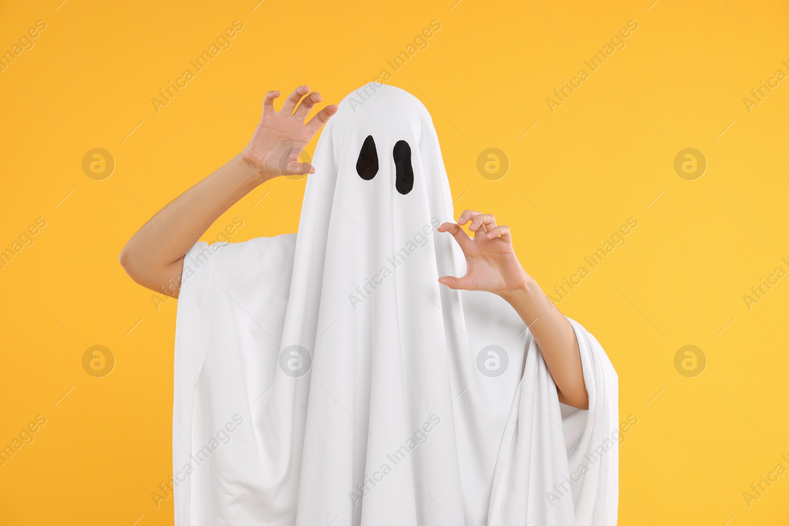 Photo of Woman in white ghost costume on yellow background. Halloween celebration