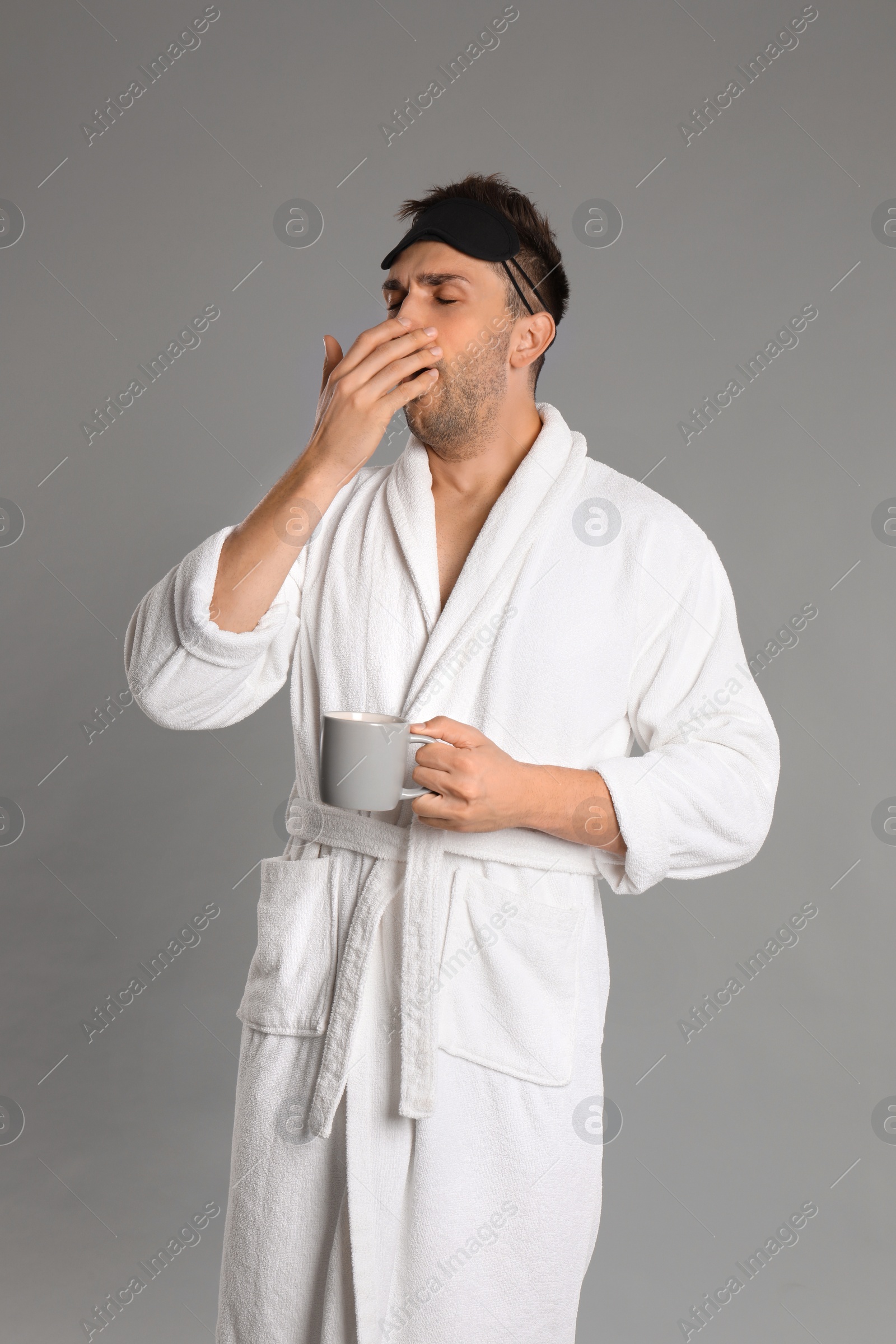 Photo of Young man in bathrobe yawning on grey background