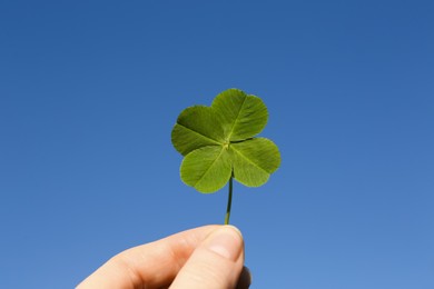 Photo of Woman holding one beautiful green clover leaf against blue sky, closeup