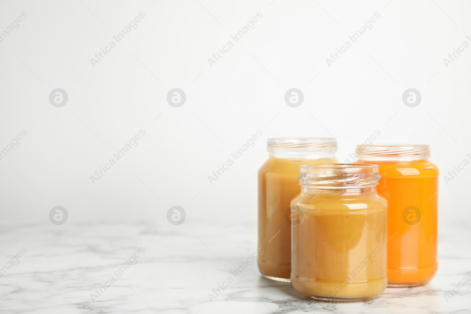 Photo of Healthy baby food in jars on marble table against white background, space for text