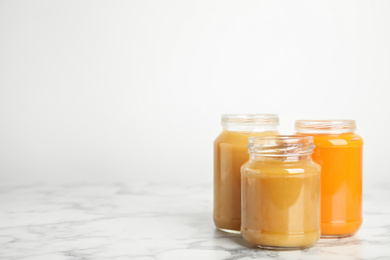 Photo of Healthy baby food in jars on marble table against white background, space for text