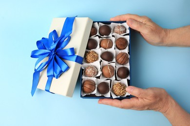 Woman with box of delicious chocolate candies on light blue background, top view