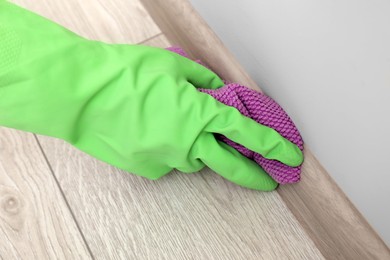 Photo of Woman in protective glove cleaning plinth with washcloth indoors, closeup