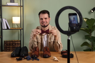 Photo of Smiling fashion blogger showing men's accessories while recording video at home