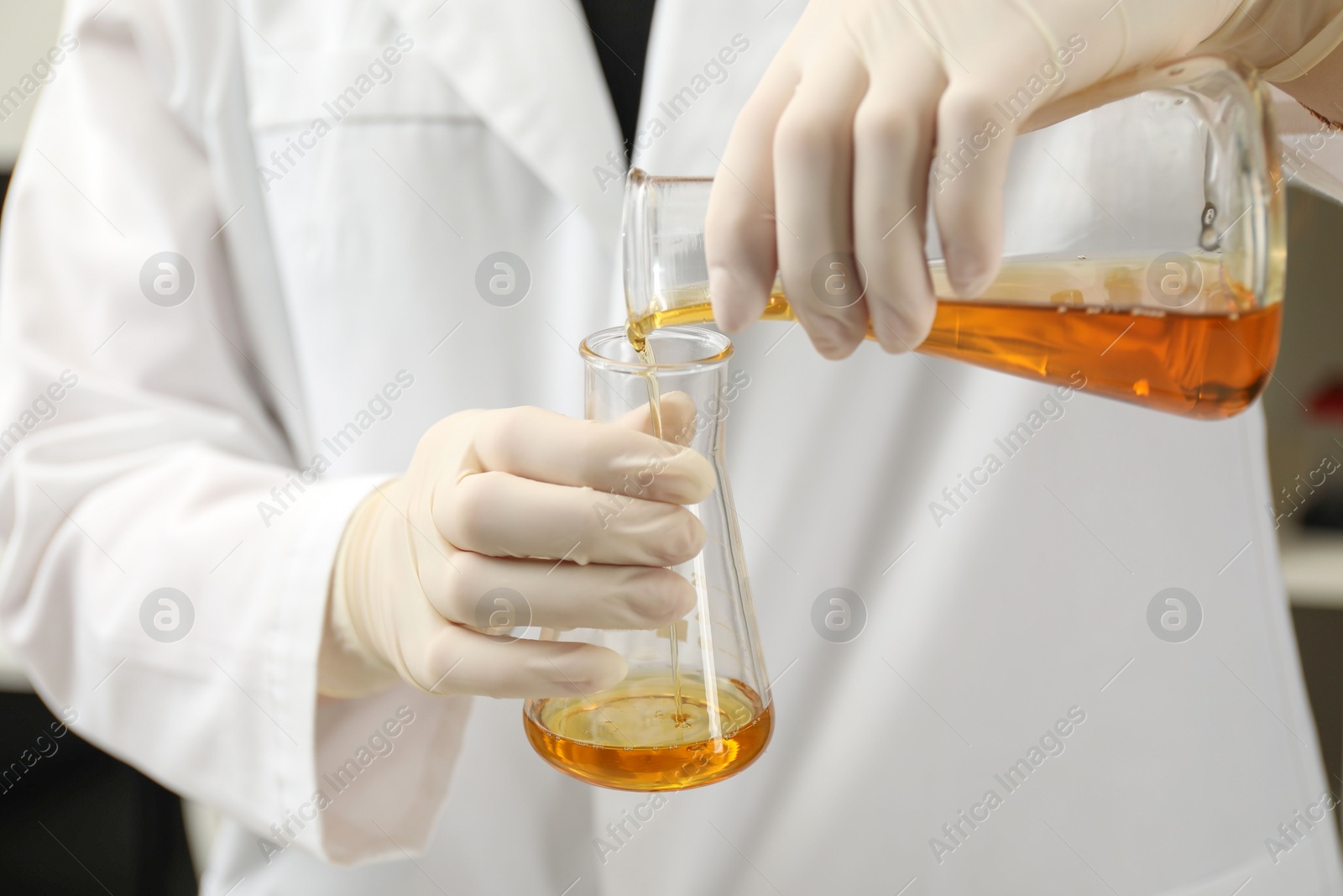 Photo of Laboratory worker pouring orange crude oil into flask, closeup