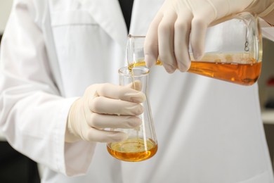 Photo of Laboratory worker pouring orange crude oil into flask, closeup