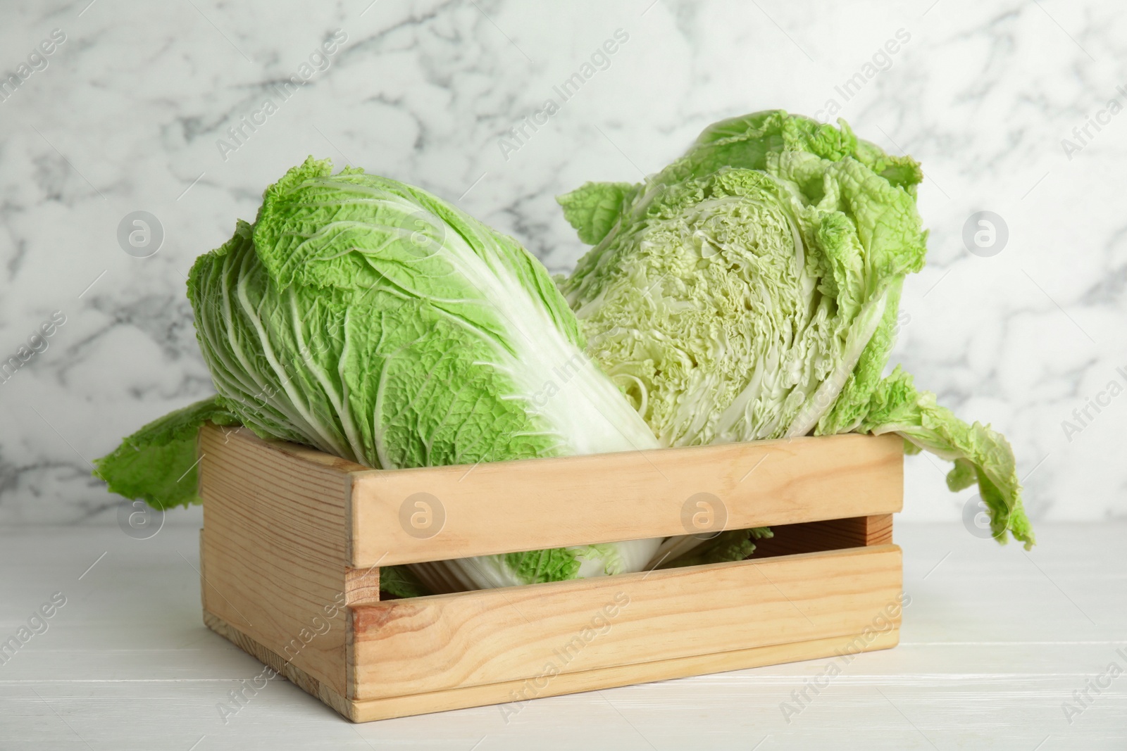 Photo of Chinese cabbages in wooden crate on white table
