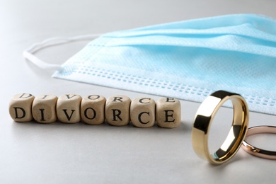 Photo of Cubes with word Divorce, protective mask and wedding rings on grey table