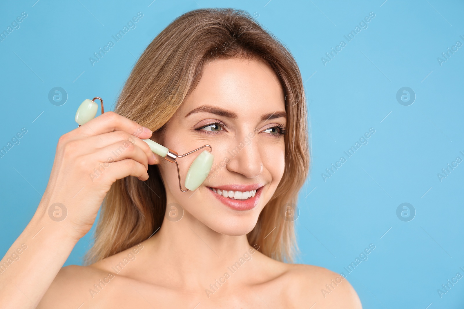 Photo of Young woman using natural jade face roller on light blue background