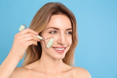 Young woman using natural jade face roller on light blue background