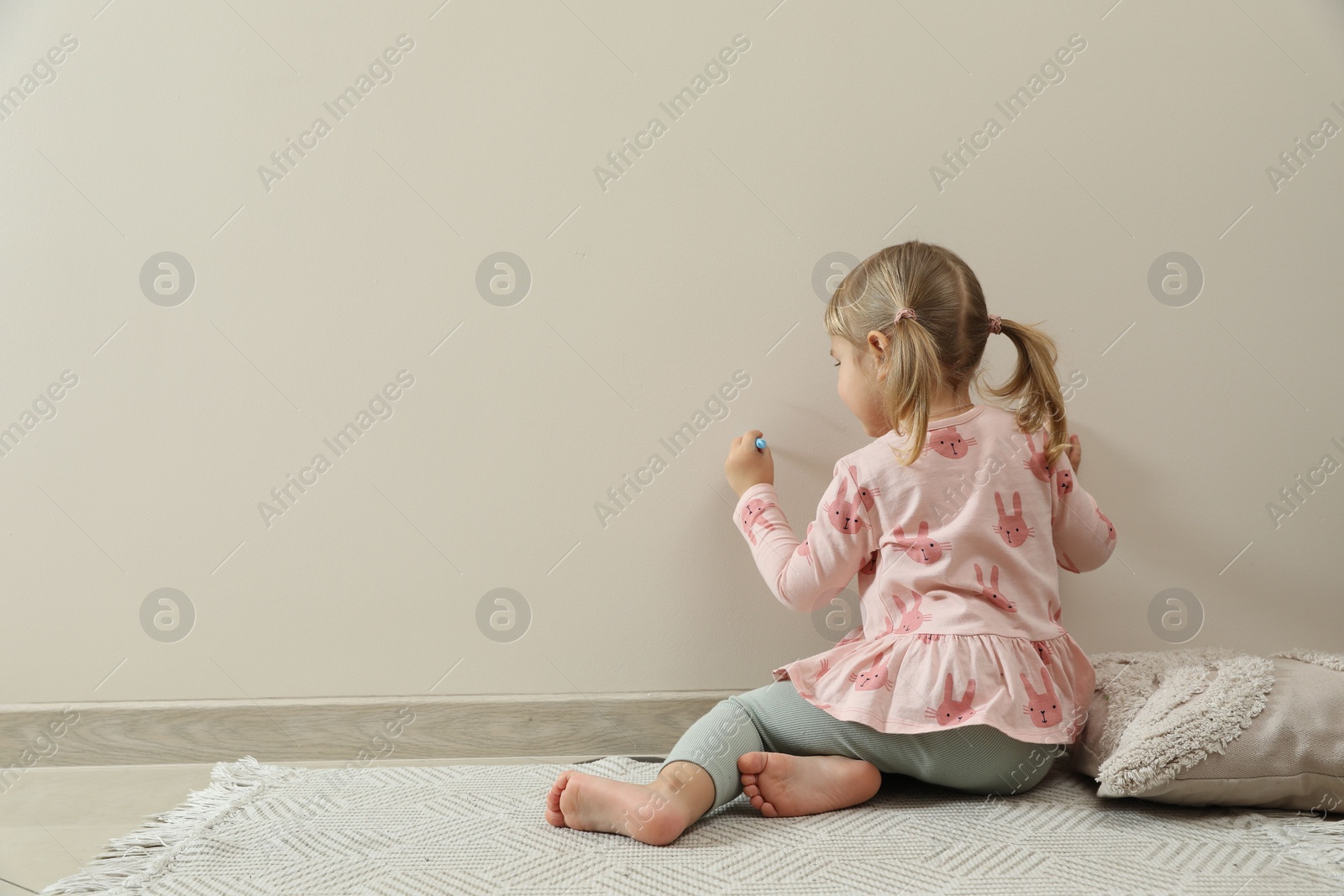 Photo of Little girl drawing on beige wall indoors, back view and space for text. Child`s art