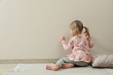 Little girl drawing on beige wall indoors, back view and space for text. Child`s art