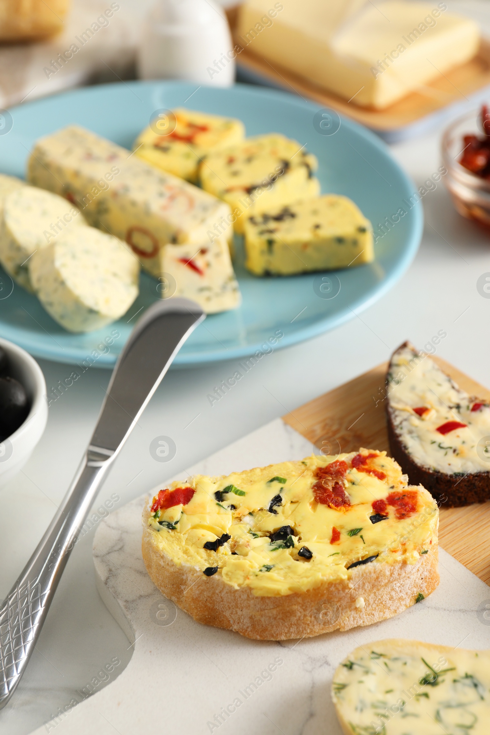 Photo of Different types of tasty butter, bread and knife on white table