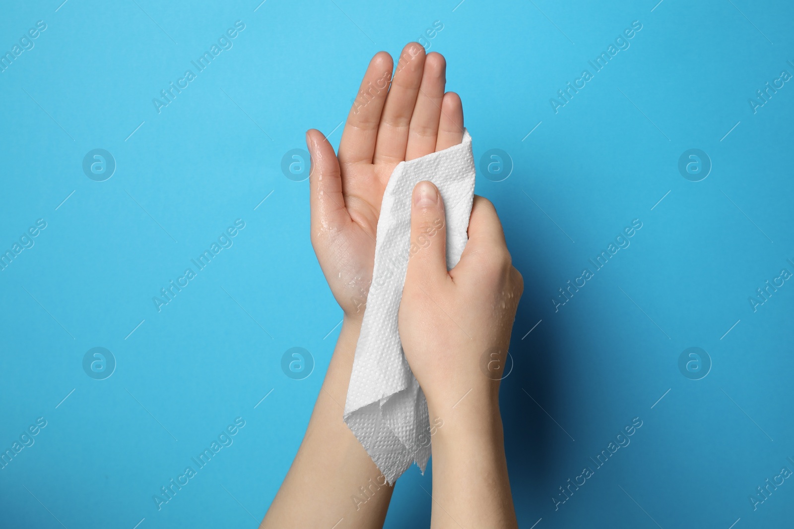 Photo of Woman wiping hands with paper towel on light blue background, closeup