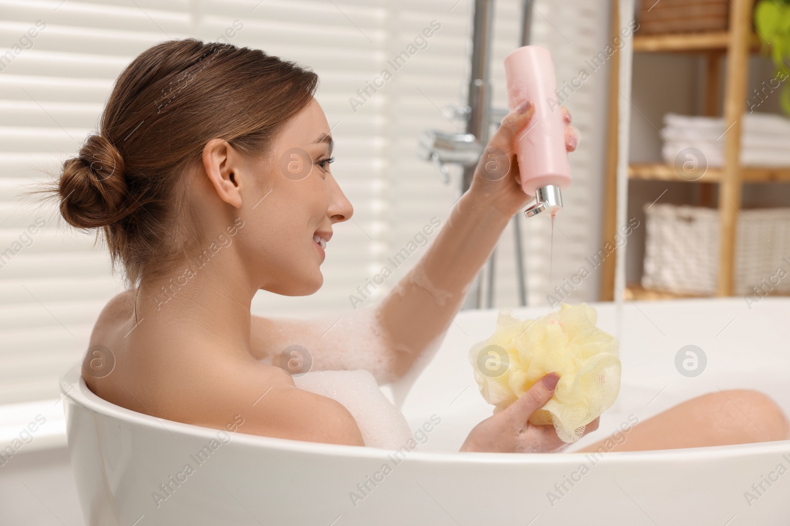 Photo of Woman pouring shower gel onto mesh pouf in bath indoors