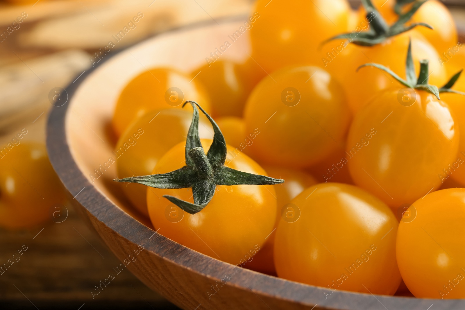 Photo of Ripe yellow tomatoes in wooden bowl, closeup