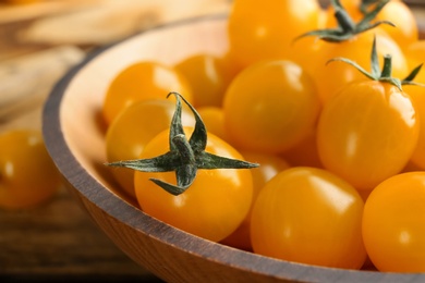 Photo of Ripe yellow tomatoes in wooden bowl, closeup