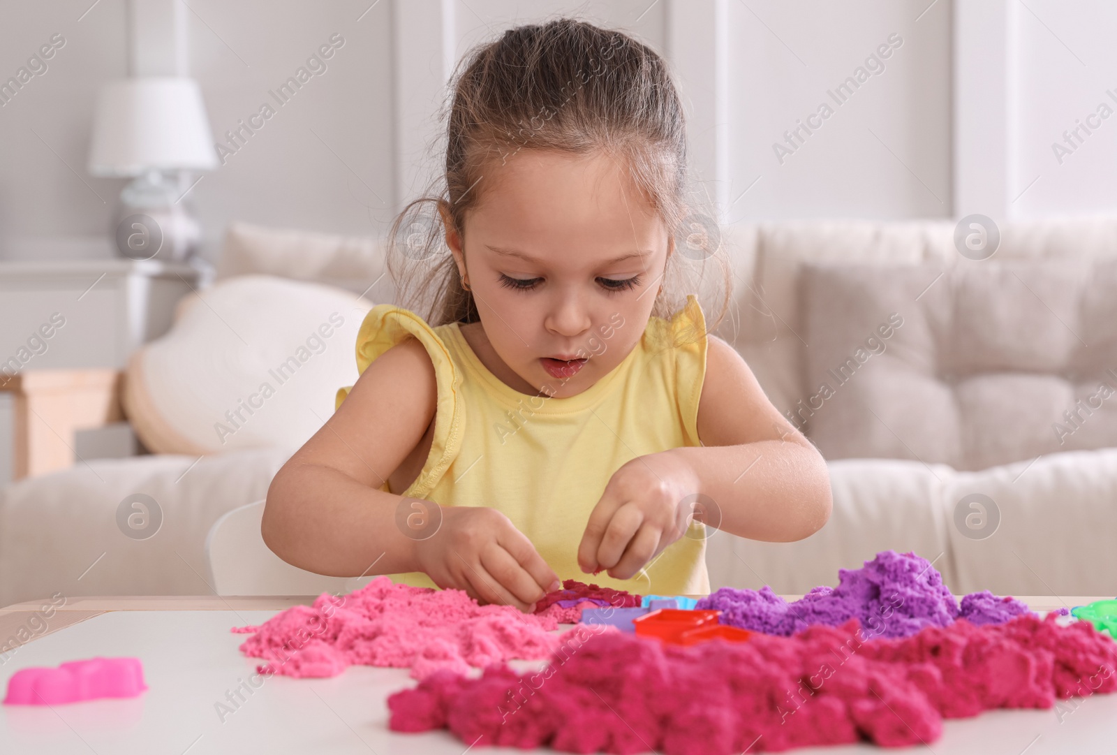 Photo of Cute little girl playing with bright kinetic sand at table in room