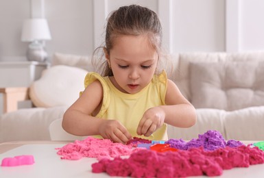 Cute little girl playing with bright kinetic sand at table in room