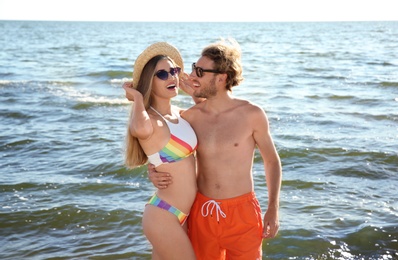 Happy young couple in beachwear spending time together at seashore on sunny day