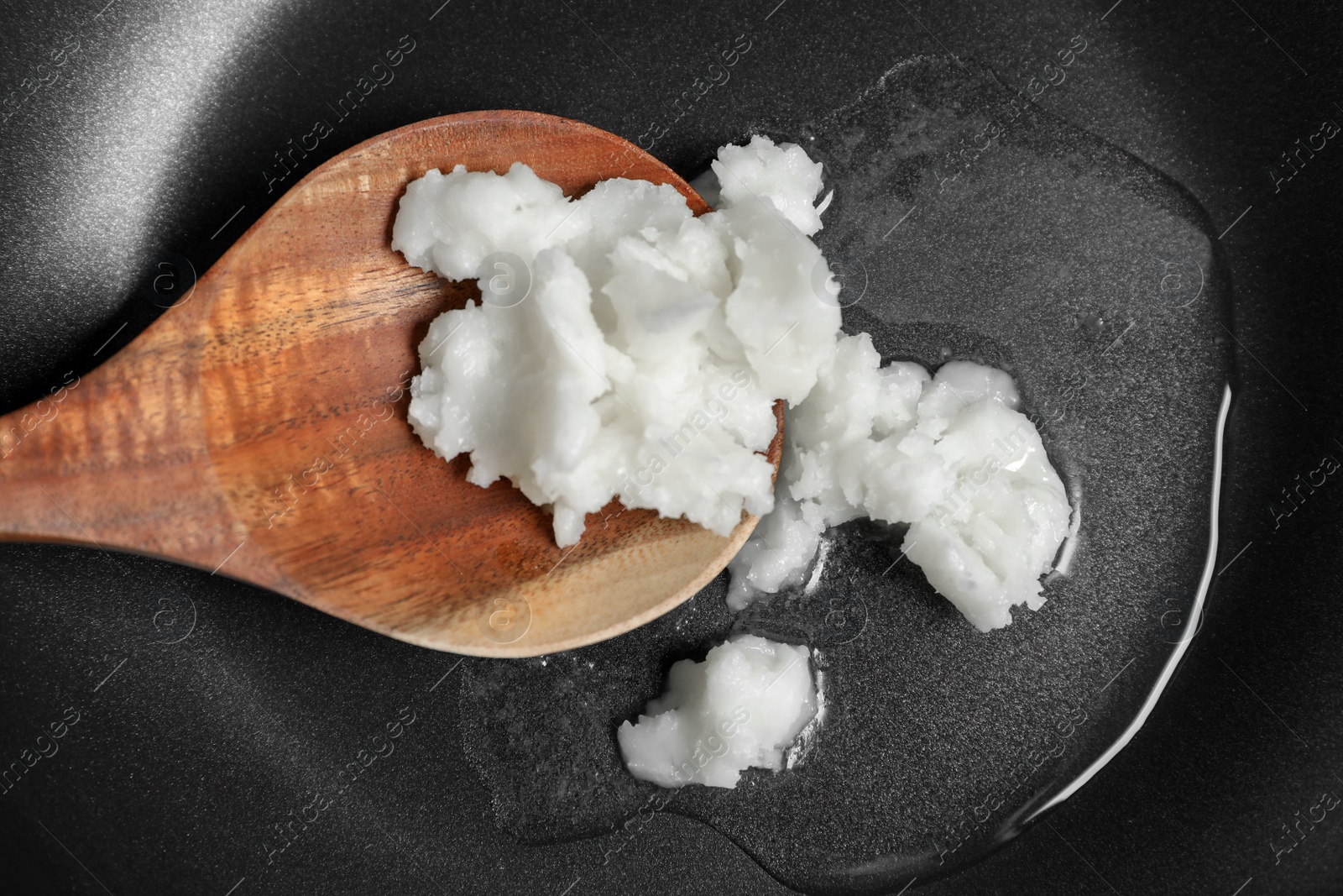 Photo of Frying pan with coconut oil and wooden spatula, top view. Healthy cooking