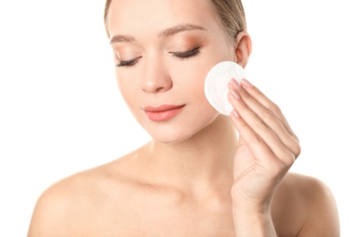 Portrait of beautiful young woman removing makeup with cotton pad on white background