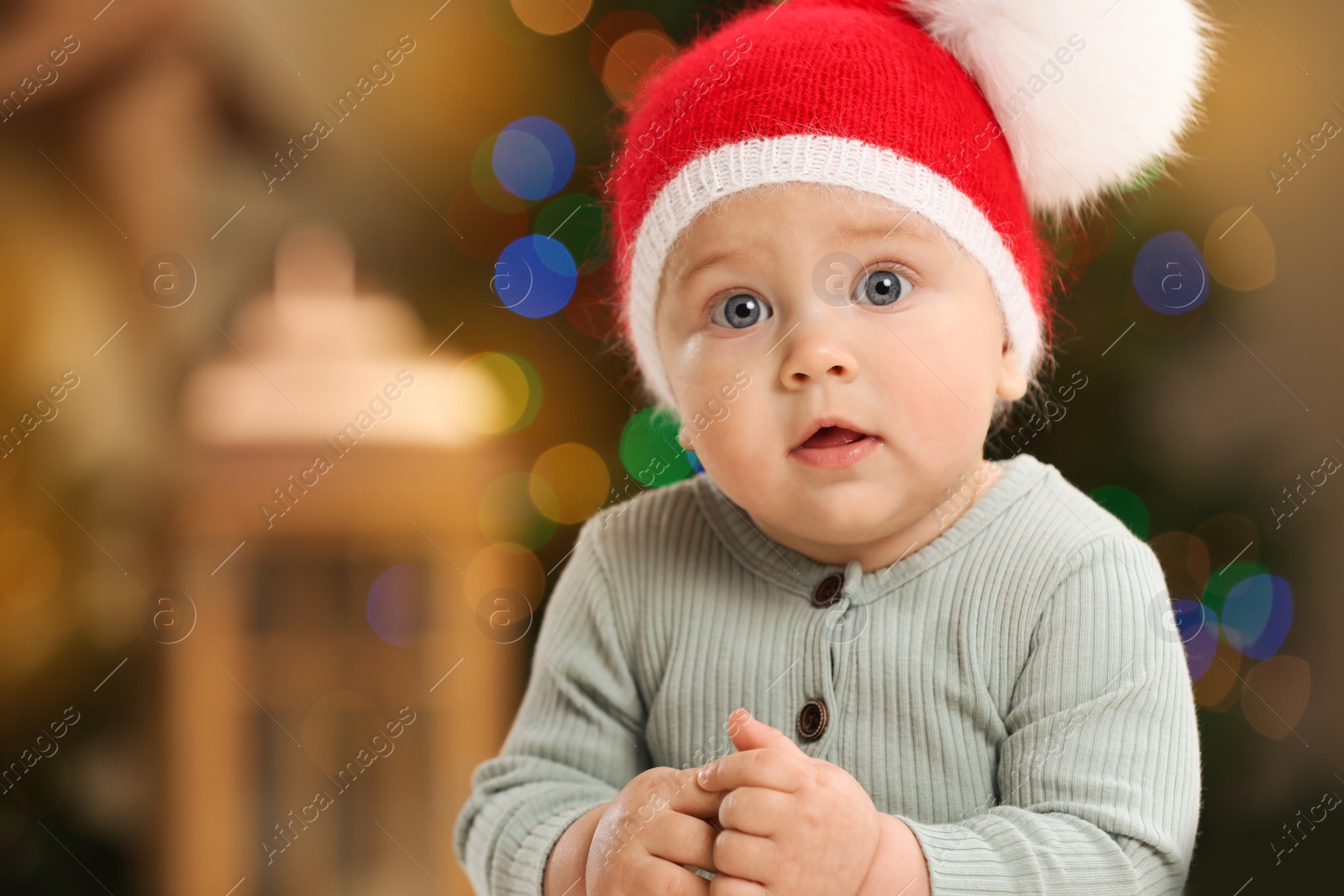 Photo of Cute little baby and blurred Christmas lights on background, space for text. Winter holiday