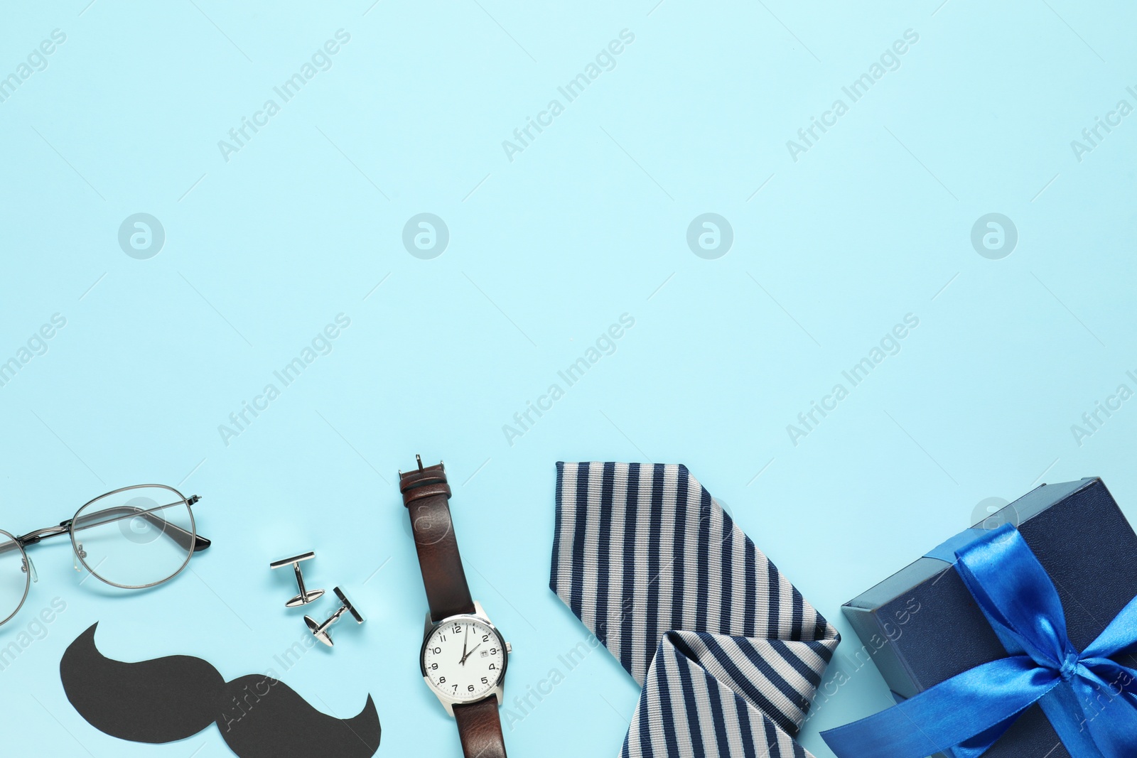 Photo of Paper mustache, gift box and men accessories on light blue background, flat lay with space for text. Father's day celebration