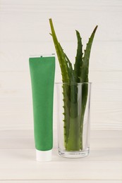 Photo of Tube of toothpaste and fresh aloe vera leaves on white wooden table