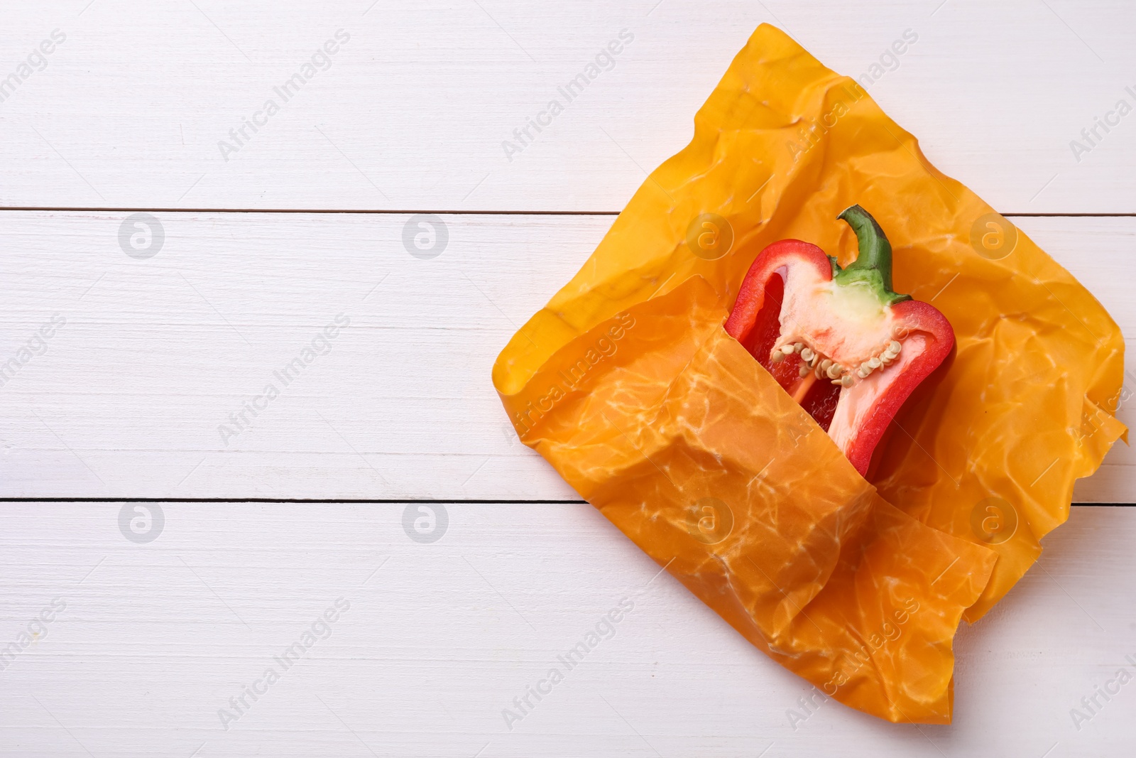 Photo of Half of bell pepper in beeswax food wrap on white wooden table, top view. Space for text