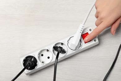 Photo of Woman pressing button of power strip on white wooden floor, top view. Space for text