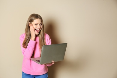 Emotional young woman with laptop celebrating victory on color background. Space for text