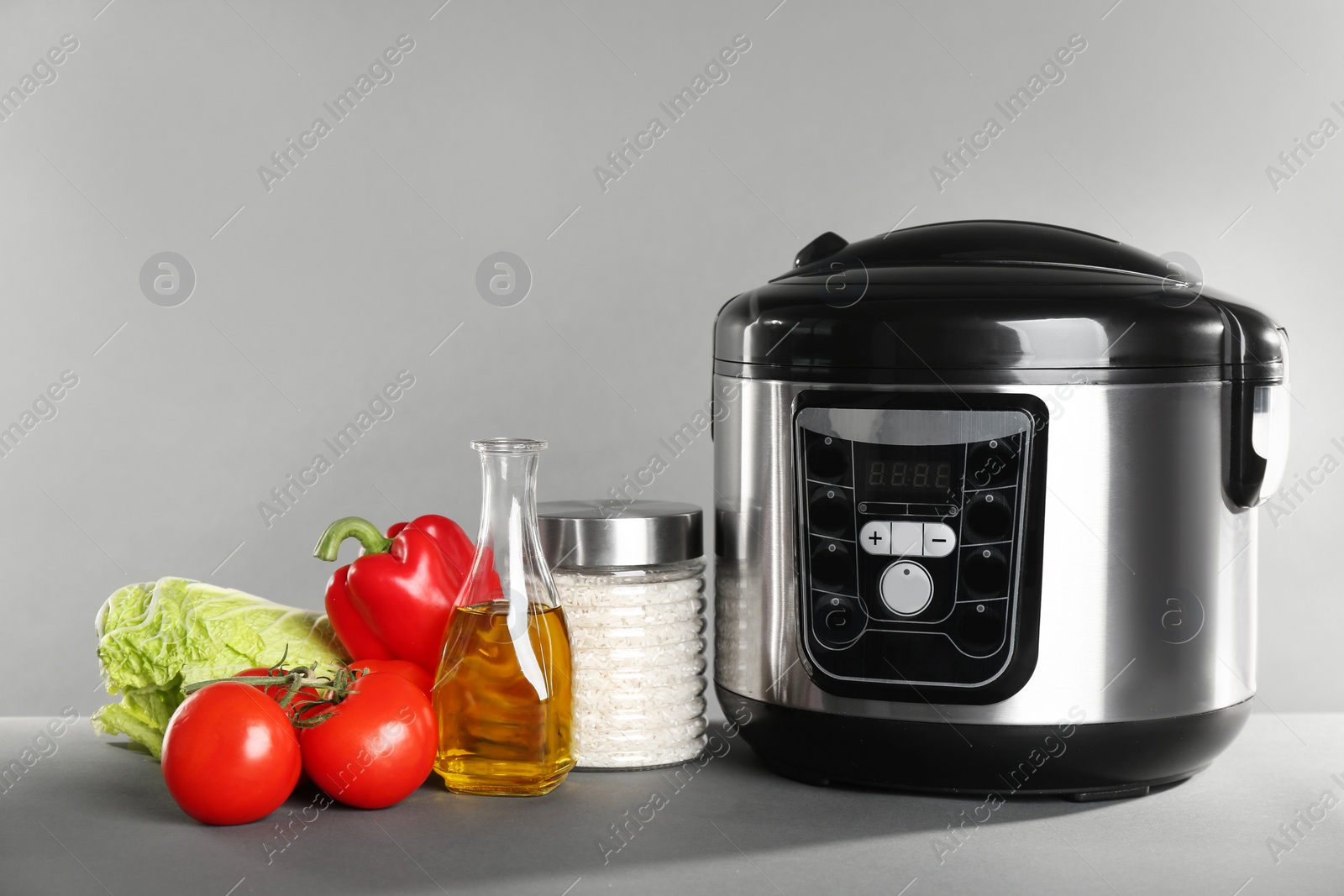 Photo of Modern multi cooker and products on table against grey background. Space for text