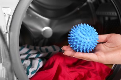 Photo of Woman putting blue dryer ball into washing machine, closeup